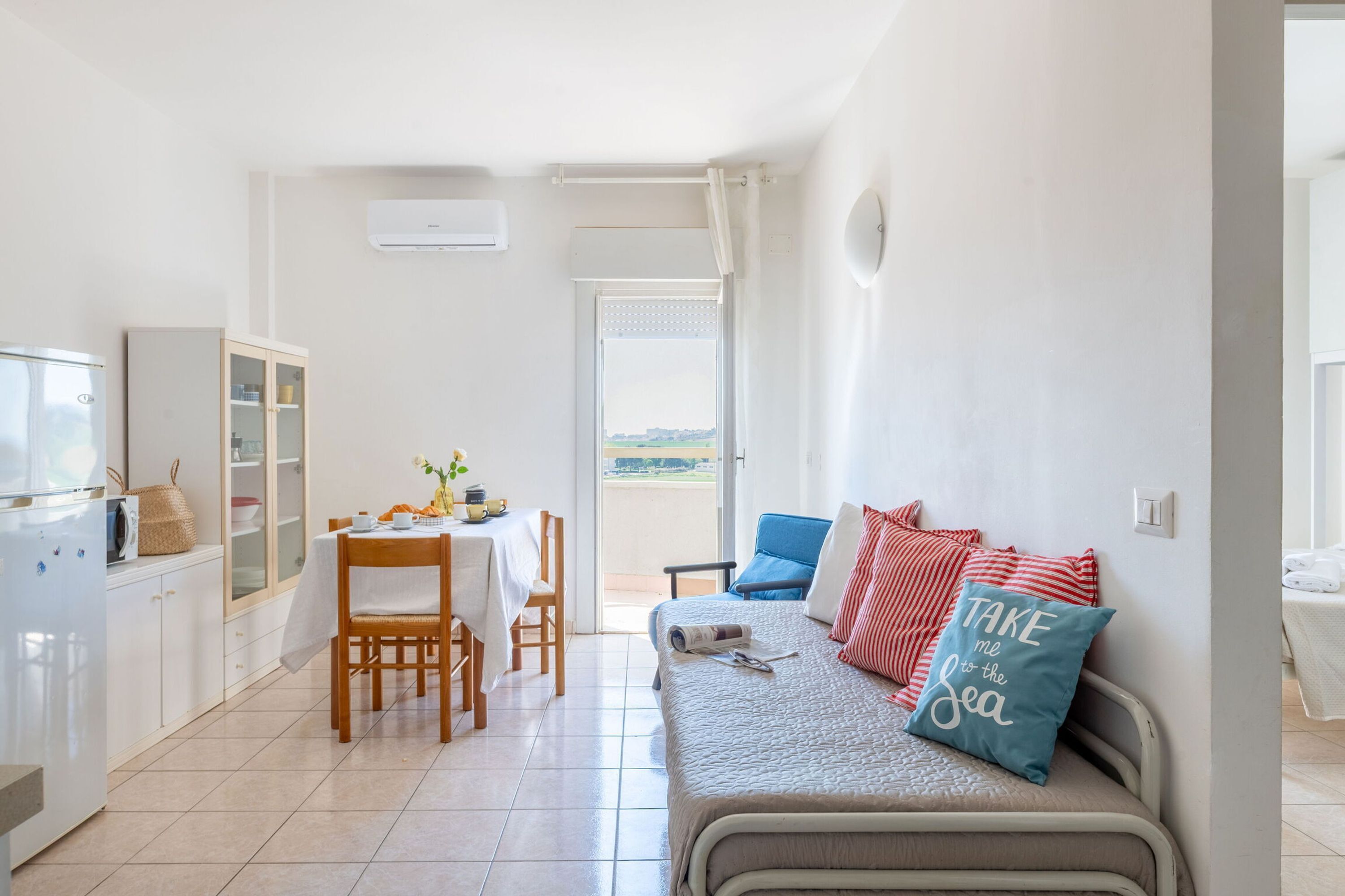 A compact living space with a kitchenette, dining area, and a sofa with decorative pillows.