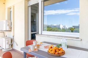 A balcony with a table set for breakfast, a basket of fruit, and a view of buildings in the distance. - Casabianca in Lido di Fermo (Fermo)