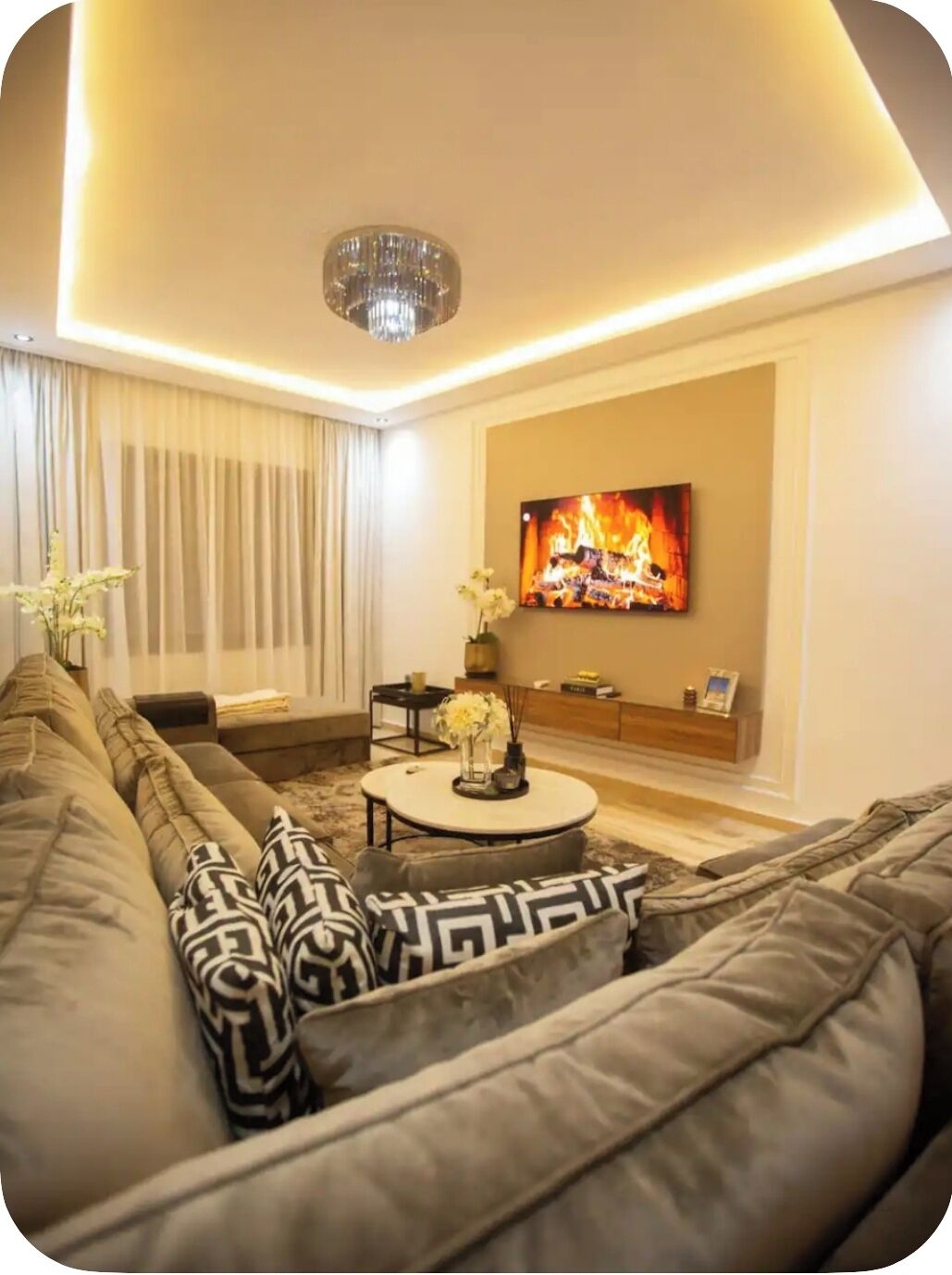 A modern living room with a large sofa, a small round table, and a flat-screen TV mounted on the wall.