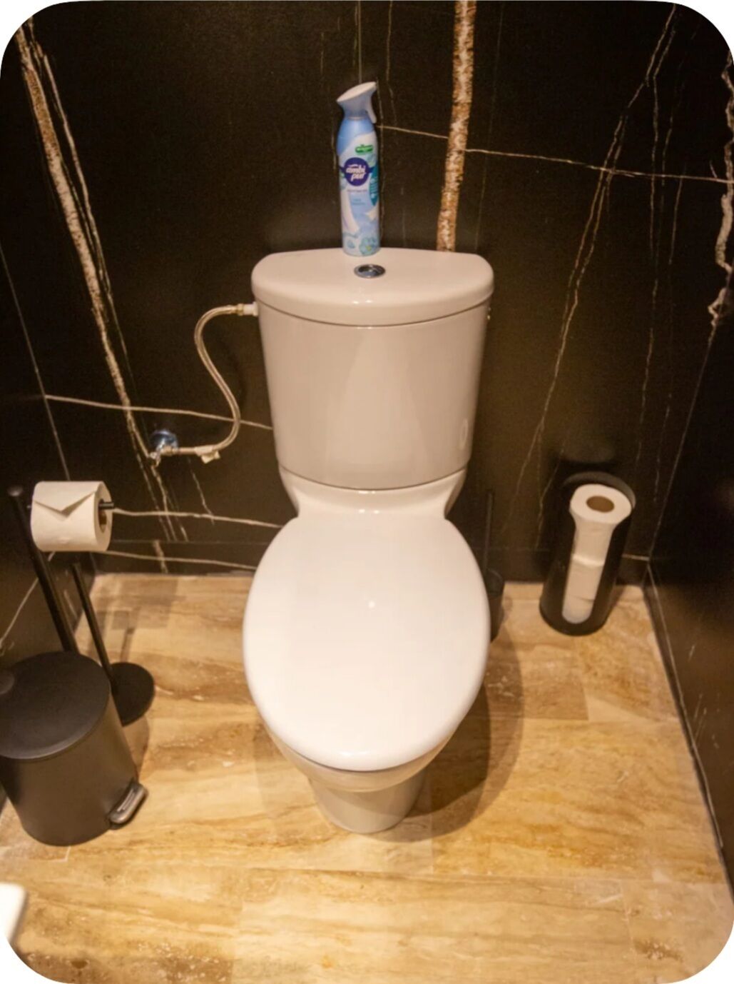 Een toilet met een toiletpapierhouder, een spuitfles voor een bidet en een rol bidetpapier.