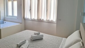 A bedroom with a bed, a window with curtains, a bedside table, and a mirror.