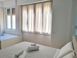 A bedroom with a bed, a window with curtains, a bedside table, and a mirror.