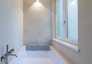 Un baño con bañera, una ventana y una pared con textura.