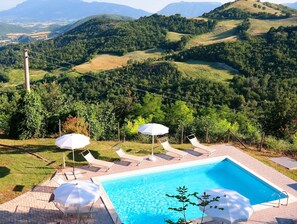Ein Pool mit Liegestühlen und Sonnenschirmen, umgeben von einer hügeligen Landschaft.
