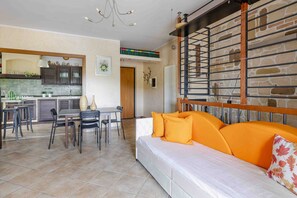 A modern living room with a sofa, dining area, kitchen, and a staircase with a stone wall. - Casa Dolceconero in Castelfidardo (Castelfidardo)
