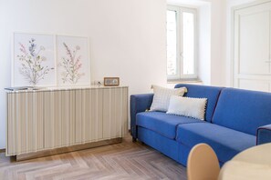 A room with a blue sofa, a radiator, and two framed floral artworks on the wall. - Suite Sinfonia Blu in Bevagna (Bevagna)