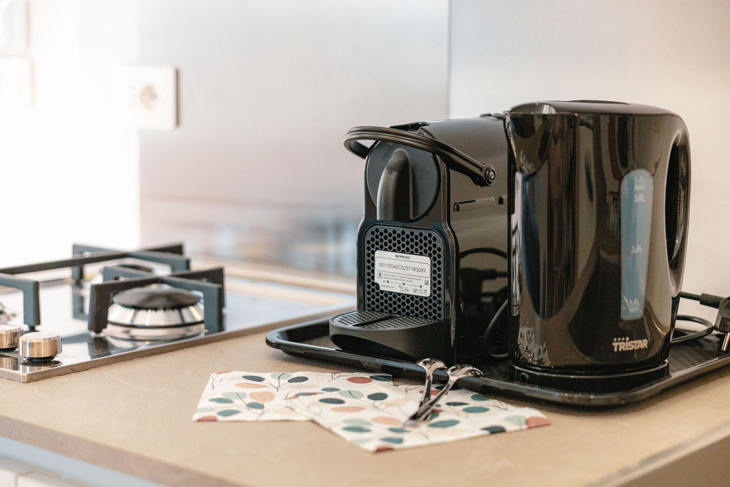 A coffee maker and a kettle on a kitchen counter with a window in the background.