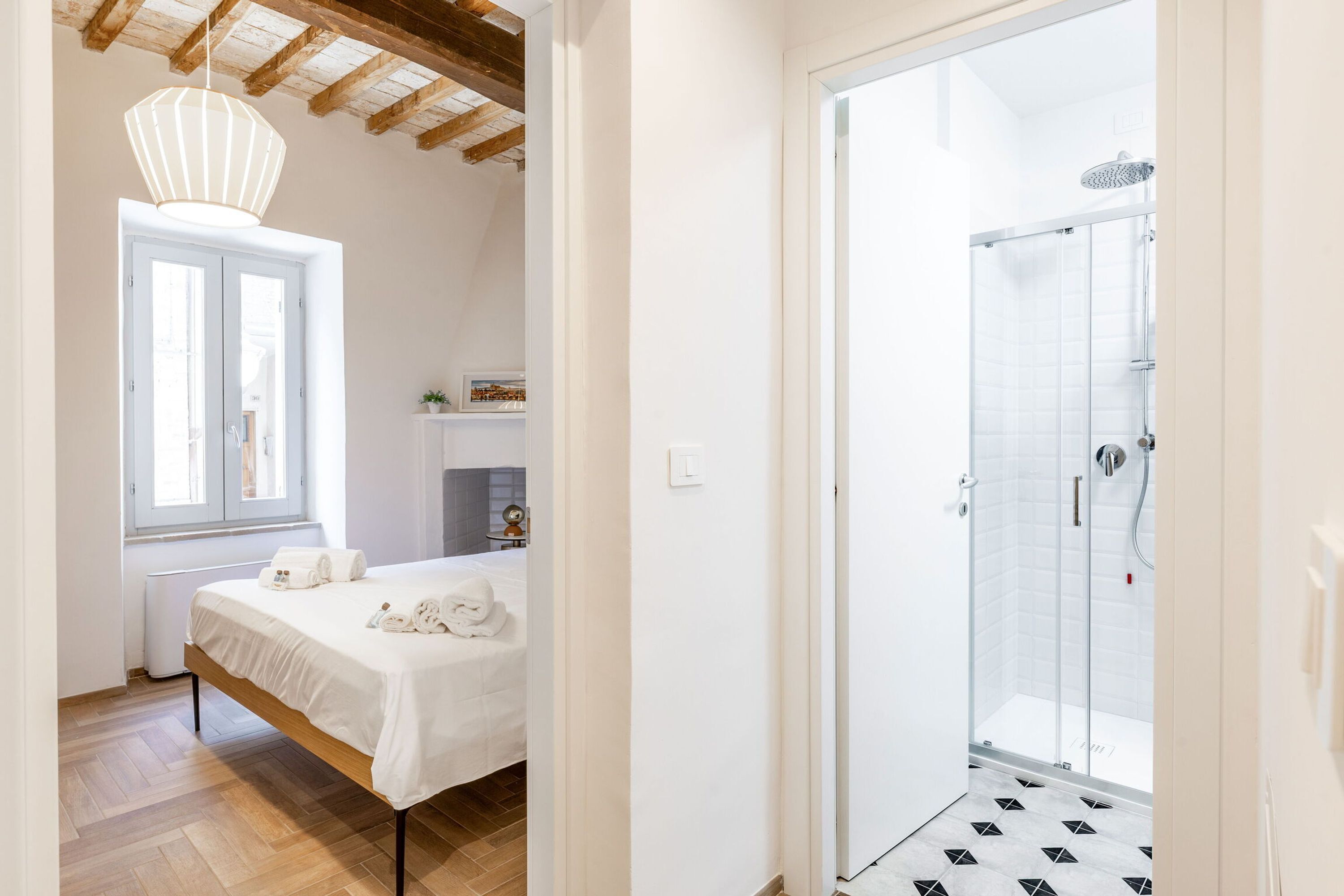 A hotel room with a bed, a window, a shower, and a wooden floor.