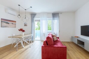 Uma sala de estar moderna com um sofá vermelho, uma mesa de jantar com cadeiras, uma TV de tela plana e um quadro na parede.