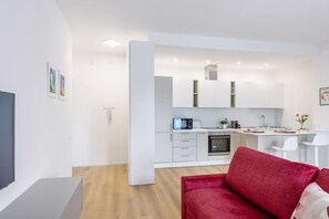 Um apartamento moderno com sala de estar que inclui um sofá vermelho, cozinha com armários brancos, área de refeições e uma TV de tela plana.