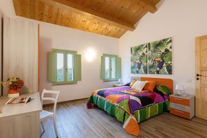 A bedroom with a wooden ceiling, a bed with a colorful quilt, a desk with a chair, and a window with shutters. - Zena Suite in Cingoli (Cupramontana)