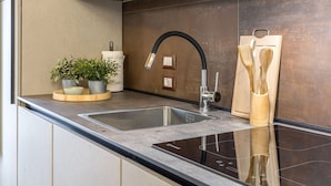 Ett modernt kök med en diskho i rostfritt stål, en svart blandare och en skärbräda i trä med tillhörande köksredskap.