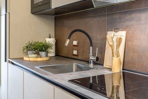 A modern kitchen with a stainless steel sink, a black faucet, and a wooden cutting board with utensils. - Zena Suite in Cingoli (Cupramontana)