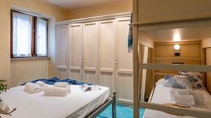 Een hotelkamer met stapelbedden, een garderobe, een raam met gordijnen en een nachtkastje met een lamp.