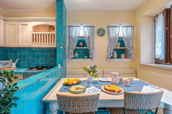 A kitchen with a blue tiled backsplash, white cabinets, and a dining table set with plates, glasses, and a vase with flowers. - Suite la Torre in Numana (Numana)