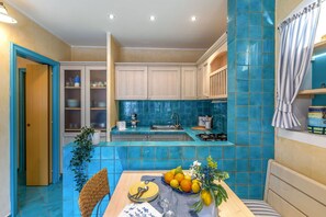 A kitchen with blue tiles, a dining table with a fruit bowl, and a wicker chair. - Suite la Torre in Numana (Numana)