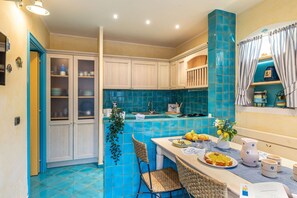 A kitchen with a blue tiled backsplash, white cabinets, and a dining area with a table set for two. - Suite la Torre in Numana (Numana)
