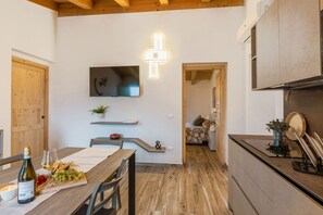 A modern kitchen with wooden beams, a dining area with a table set for a meal, and a TV mounted on the wall. - Zena Apartment in Cingoli (Cupramontana)