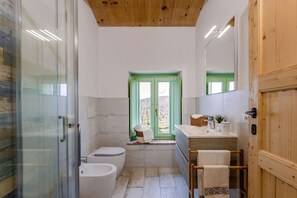 A bathroom with a glass shower enclosure, a toilet, a bathtub, a sink with a mirror, and a window with a green frame. - Zena Apartment in Cingoli (Cupramontana)