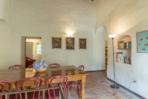 A dining area with a wooden table, red chairs, and a vase of flowers. There are three framed pictures on the wall and a bookshelf with books. - Villa Linchiano - Villa Linchiano 11 (Gambassi Terme)