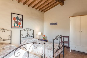 A bedroom with two metal-framed beds, a nightstand with a lamp, a chair, a wardrobe, and a painting on the wall. - Villa Linchiano - Villa Linchiano 11 (Gambassi Terme)