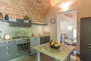 A kitchen with a brick wall, a clock, and a fruit bowl on the table. - Villa Linchiano - Villa Linchiano 11 (Gambassi Terme)
