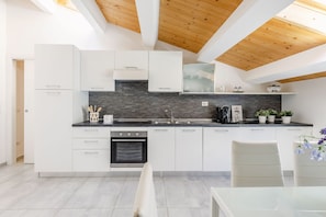 A modern kitchen with white cabinetry, a black countertop, and a wooden ceiling. - Seaside Apartment in Porto Potenza Picena (Potenza Picena)