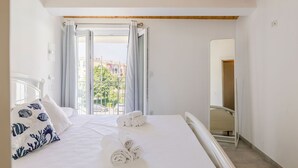 Hotellihuone, jossa on sänky, ikkuna verhoilla, näkymä ulkona oleviin rakennuksiin ja peili seinällä.