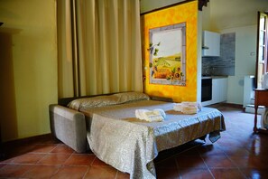 A single bed with a patterned bedspread, a bedside table with a towel, and a painting of a vineyard on the wall. - Podere Vallino - Suite Lavanda (Castelfiorentino)