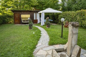 A garden with a stone pathway leading to a wooden cabin with a yellow-striped awning and a white canopy. - Podere Vallino - Suite Lavanda (Castelfiorentino)