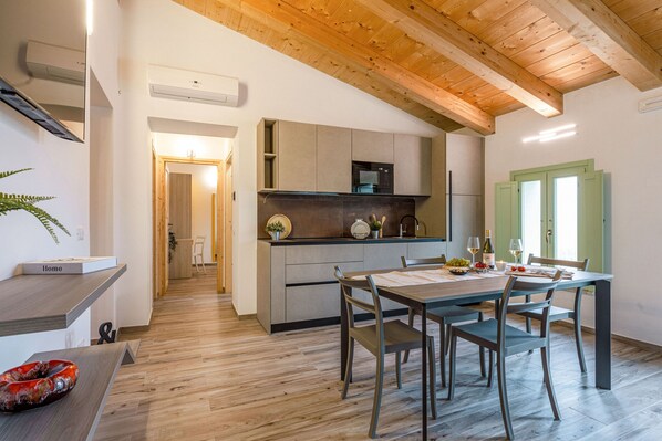A modern kitchen with wooden beams, a dining area with a table and chairs, and a view of the adjacent living space. - Villa Zena in Cingoli (Cupramontana)