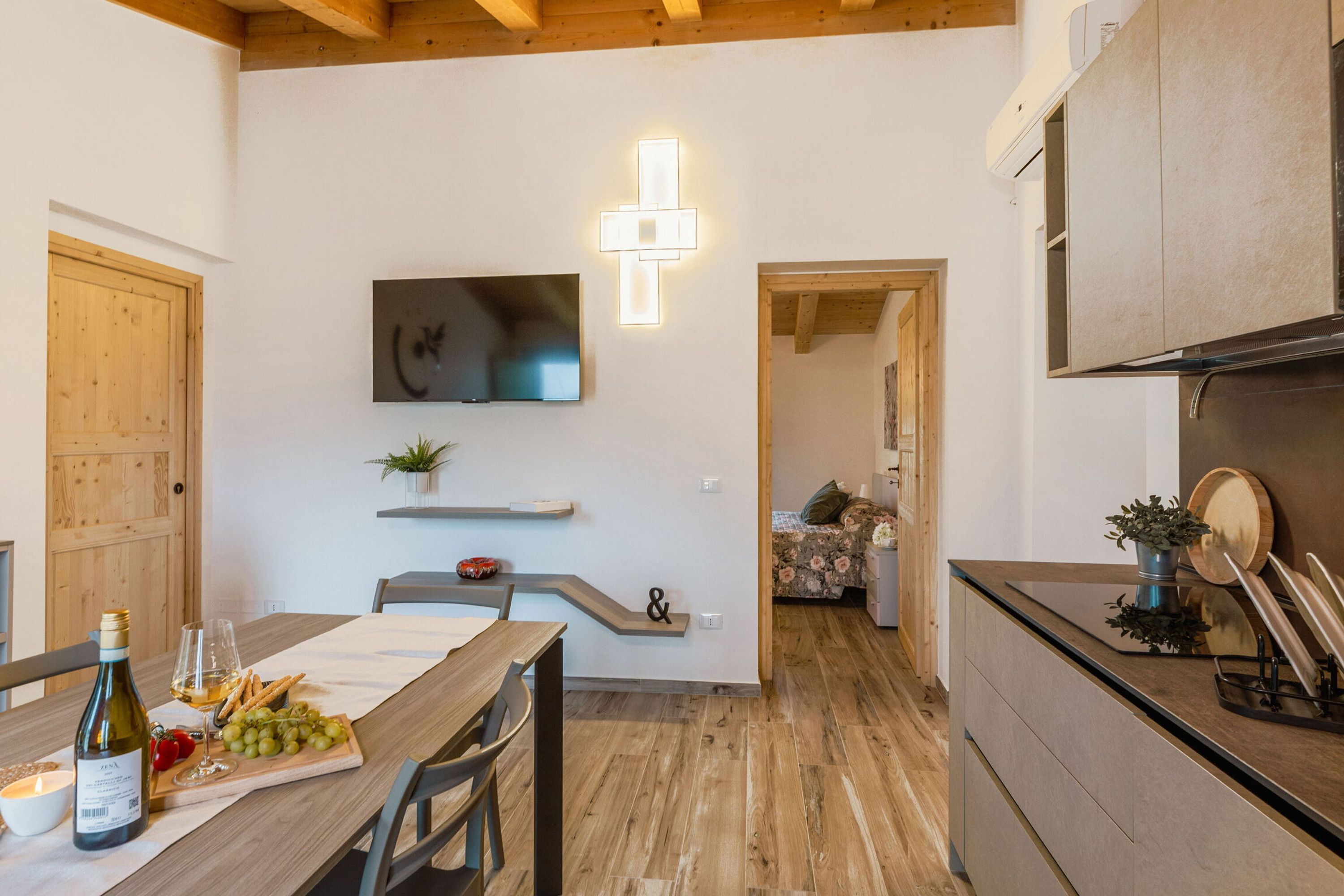 A modern kitchen with wooden beams, a dining area with a table set for a meal, and a TV mounted on the wall.