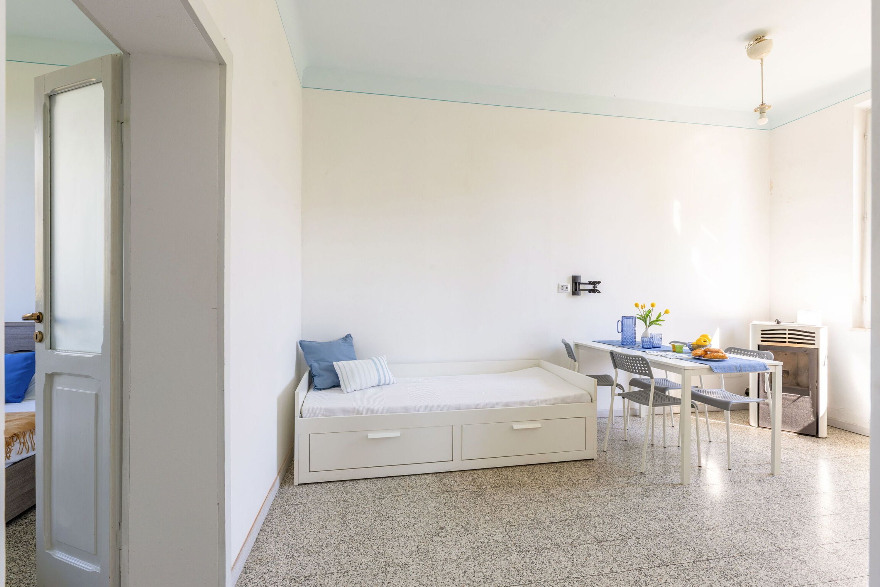 A bedroom with a bed, a desk, and a chair. There is a door on the left and a window on the right.