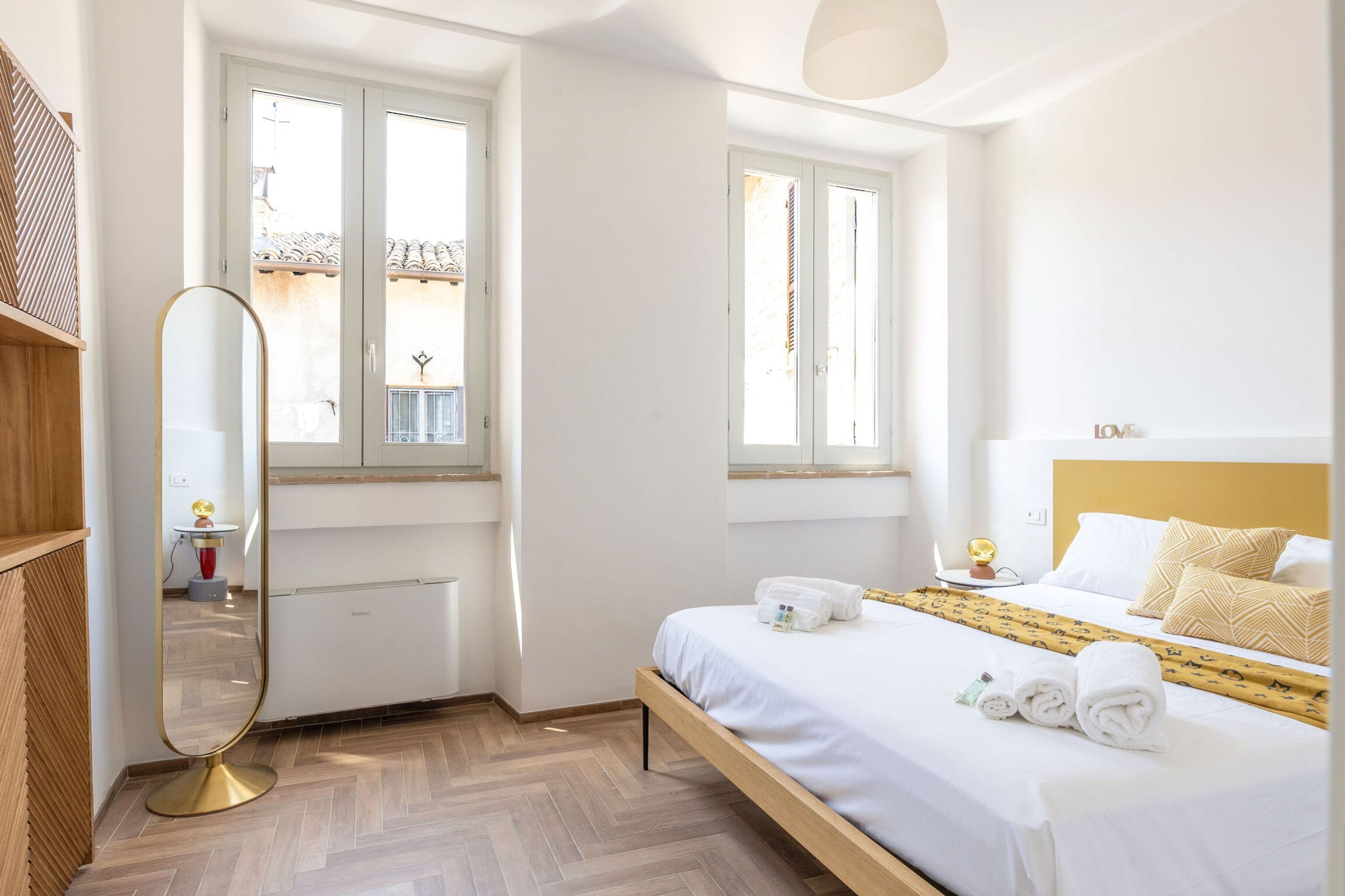 Una habitación de hotel con cama, mesita de noche y un espejo grande.