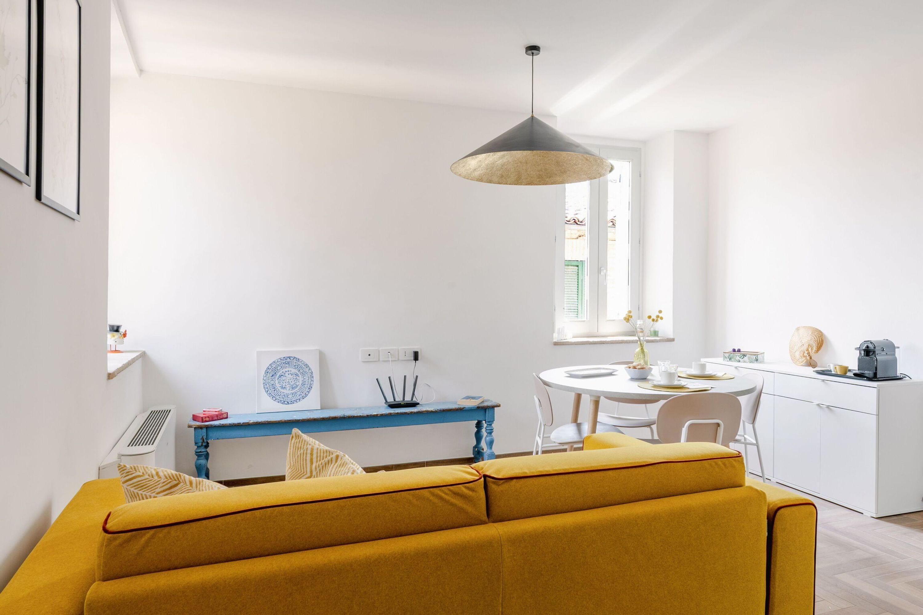 Una sala moderna con un sofá amarillo, una mesa azul y un escritorio blanco.