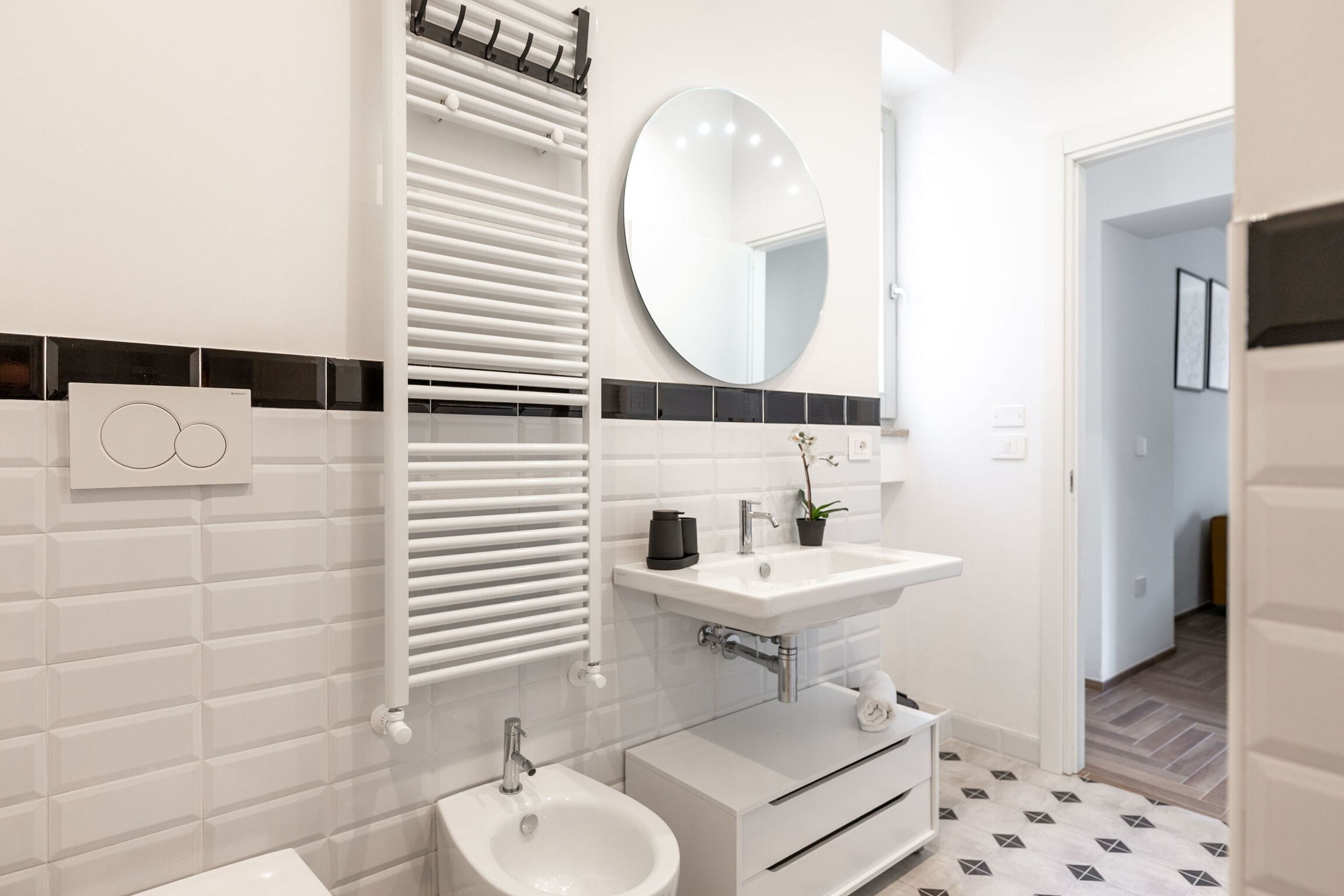 A modern bathroom with a white sink, a round mirror, and a bidet.