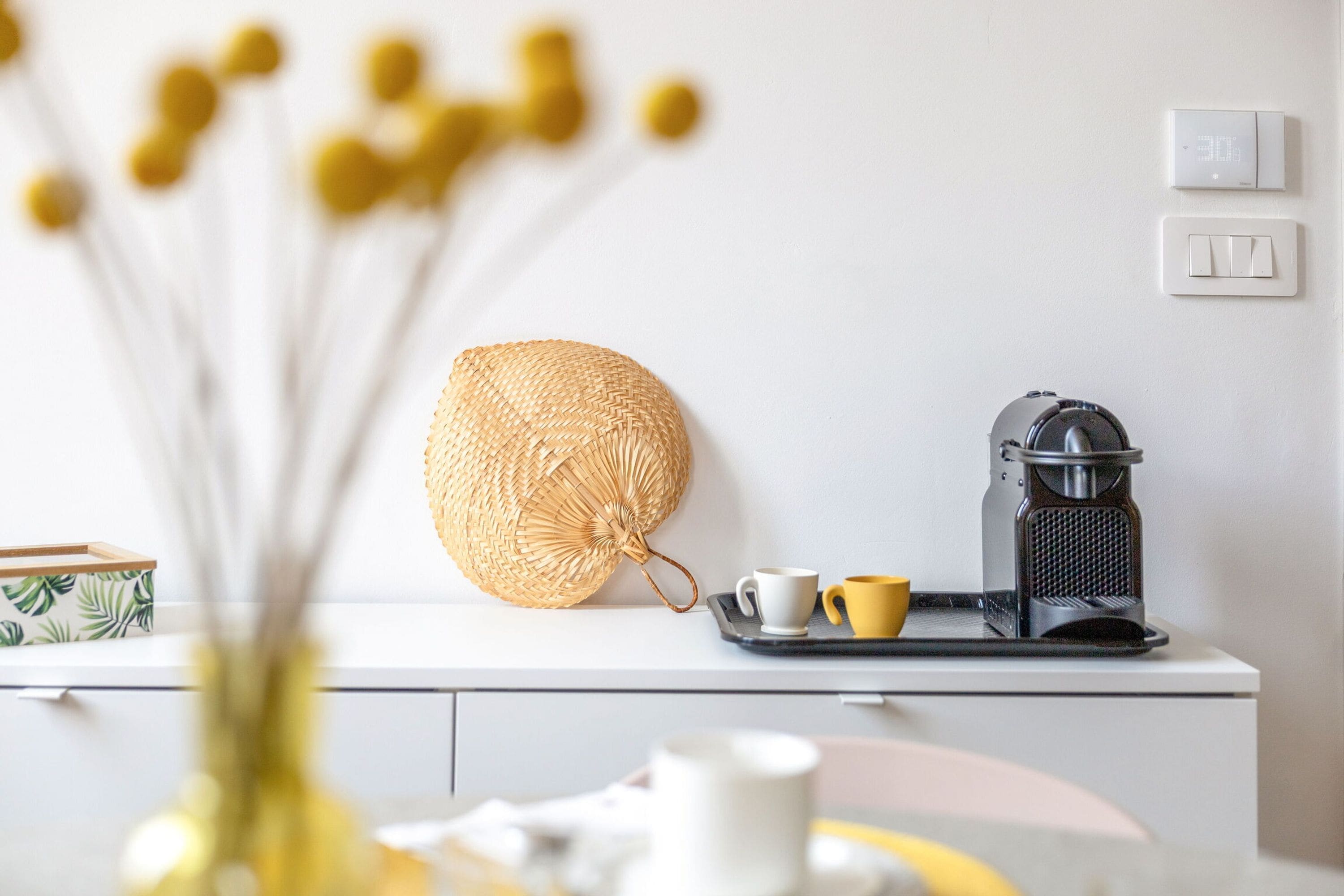 A kitchenette with a coffee maker, a tray with two cups, and a woven basket on a white counter.