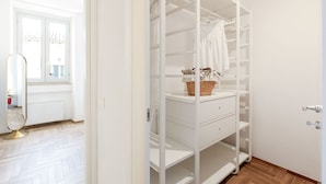 A white wardrobe with multiple shelves and drawers, a mirror, and a window with a view of the outside. - Suite Sinfonia Oro in Bevagna (Bevagna)