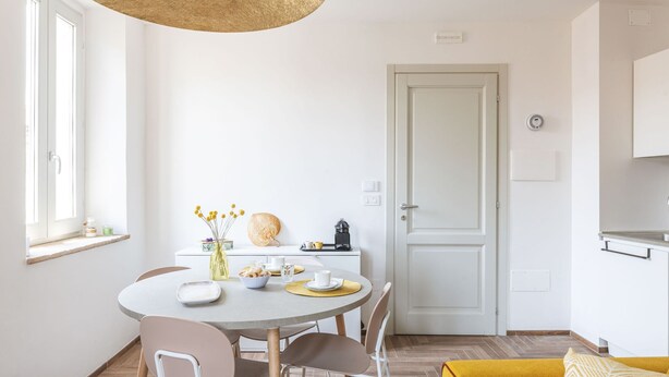 A modern kitchen with white cabinets, a dining table with chairs, and a yellow sofa. - Suite Sinfonia Oro in Bevagna (Bevagna)