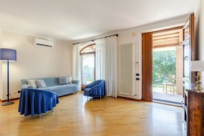 Ein Zimmer mit Holzboden, einer Couch, zwei Stühlen, einer Lampe und einem Fenster mit Vorhängen.