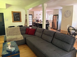 Ein modernes Wohnzimmer mit einer Eckcouch, einem kleinen Tisch mit Kerze und einer Küche im Hintergrund.