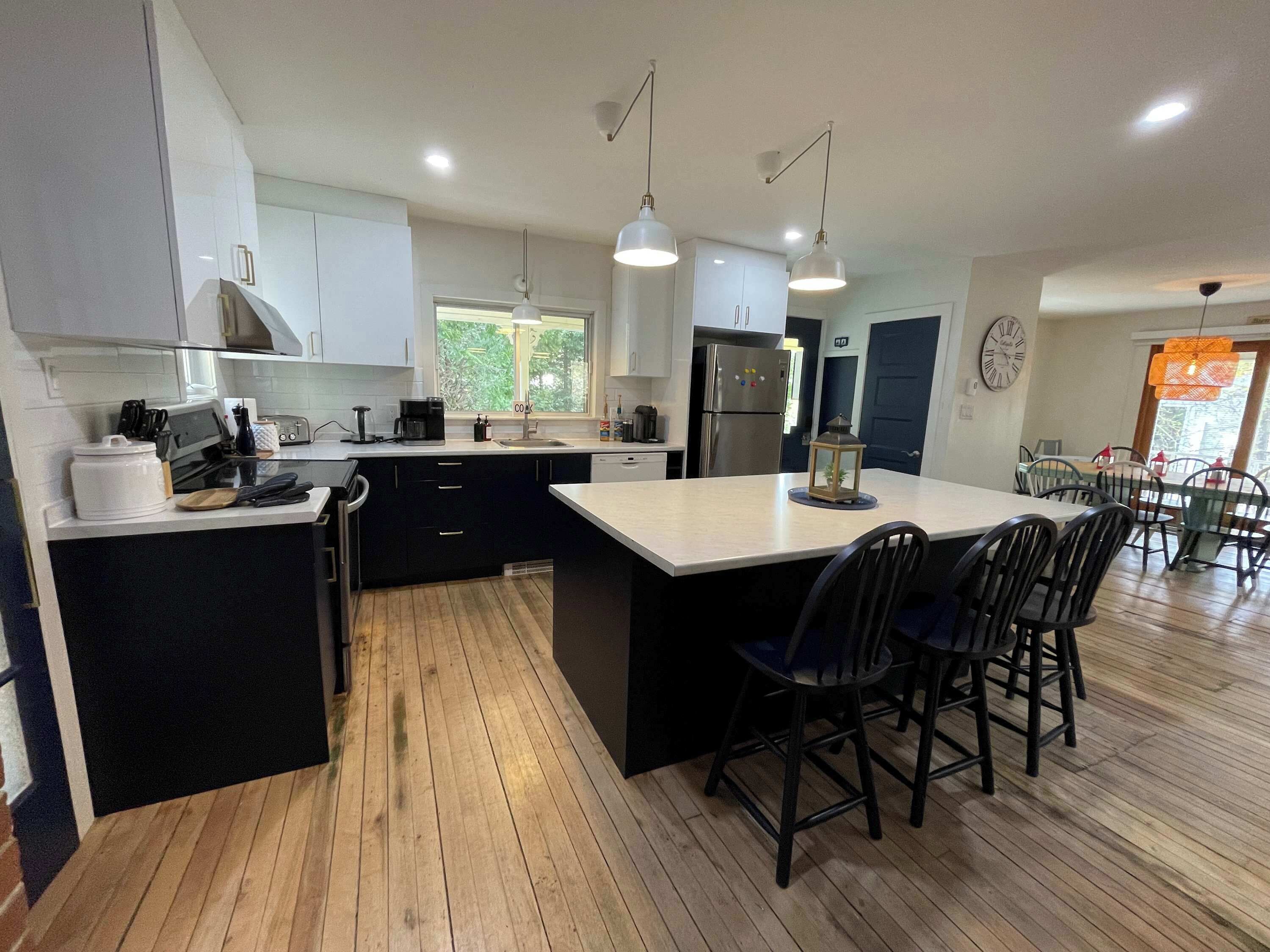 A modern kitchen with a central island, black bar stools, and a dining area with chairs and a table.