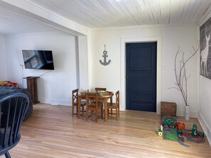 Ein Zimmer mit Holzboden, einem Esstisch mit Stühlen, einem an der Wand befestigten Fernseher und einer dunklen Tür.