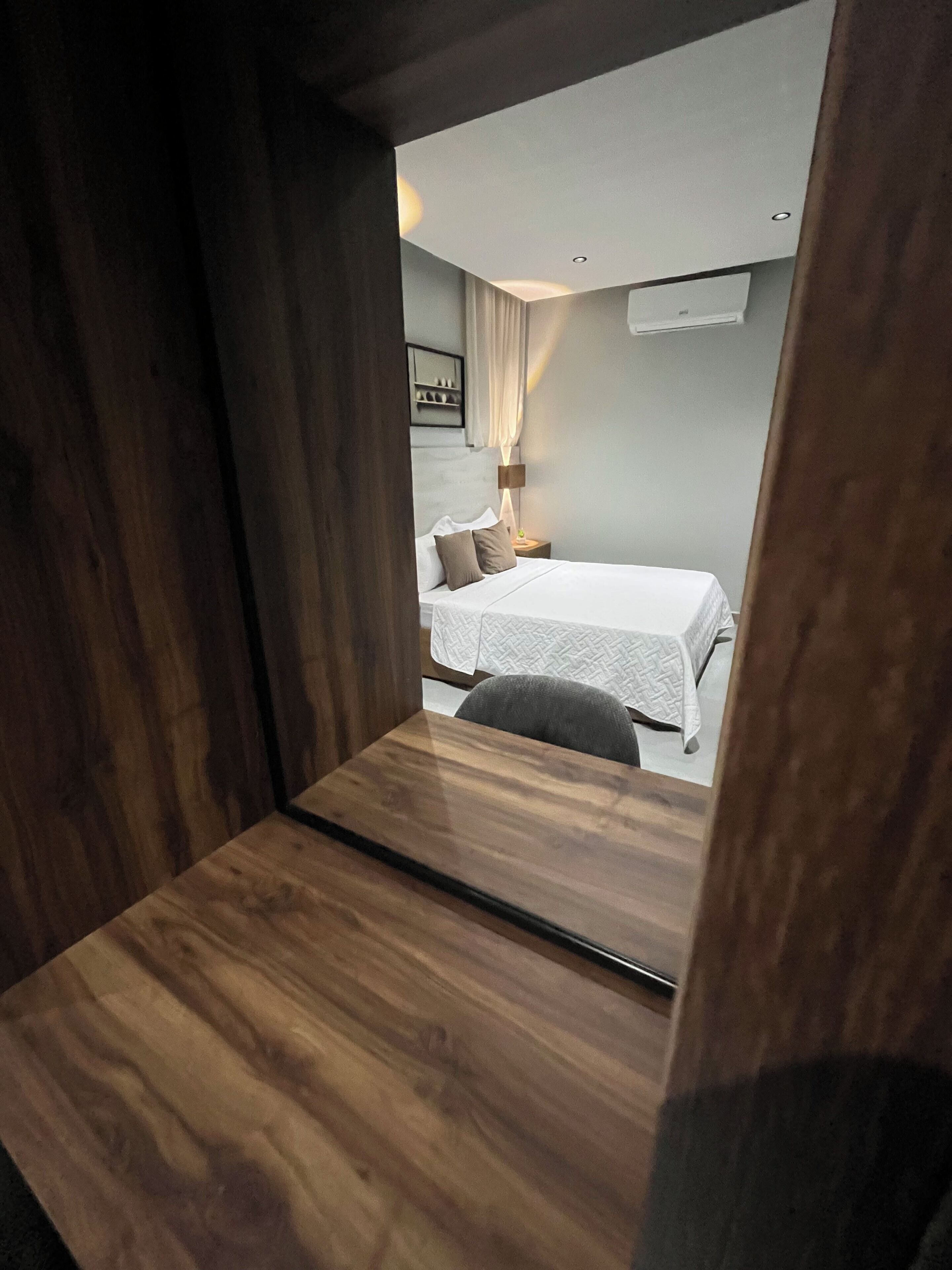 Habitación de hotel con cama, mesita de noche, lámpara y aire acondicionado instalado en la pared.