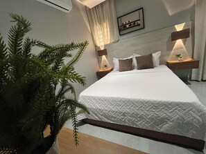 Ein Hotelzimmer mit einem Bett, einem Nachttisch mit Lampe, einer Zimmerpflanze und einem Wandregal mit Dekoration.