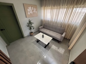 Una sala de estar con un sofá, una mesa de centro, una planta en maceta y un cuadro en la pared.