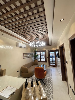Una sala de estar moderna con techo de madera, un sofá color beige, una silla naranja y un tablero de ajedrez.