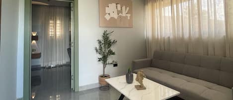 A modern living room with a sofa, a coffee table, a potted plant, and a wall art piece.