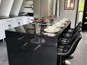 Una cocina moderna con encimera negra con vetas, armarios blancos y taburetes de cuero negro.