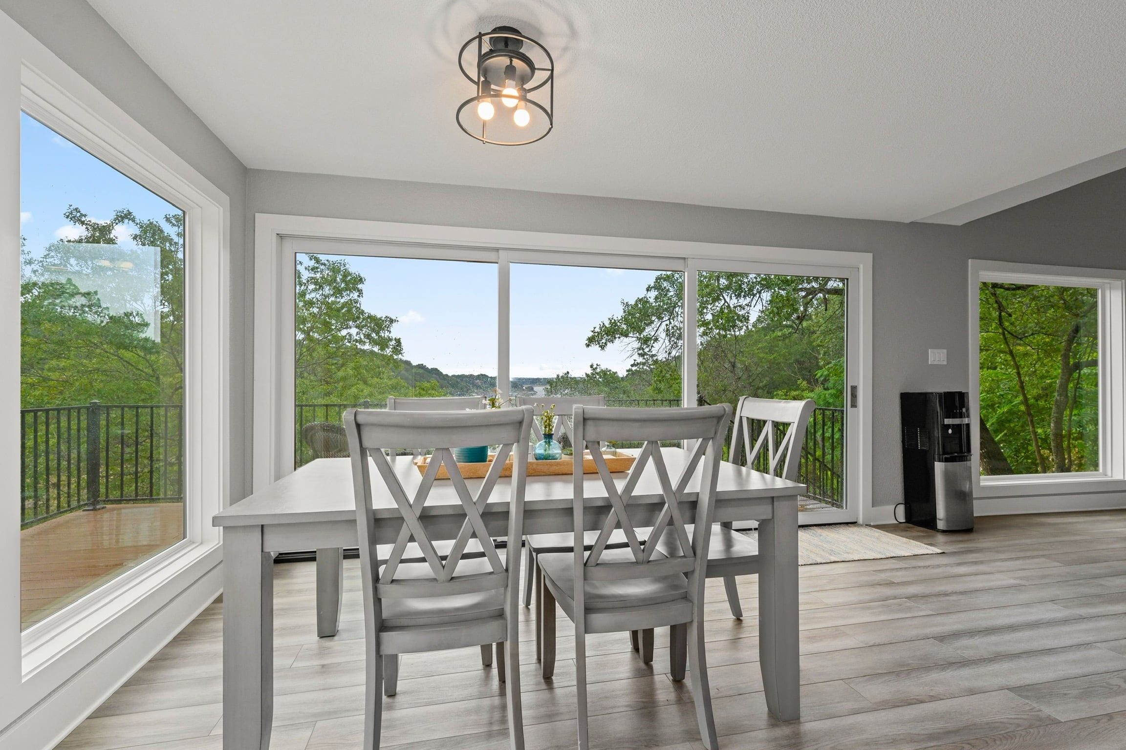 A dining area with a table and chairs, large windows, and a ceiling light fixture.